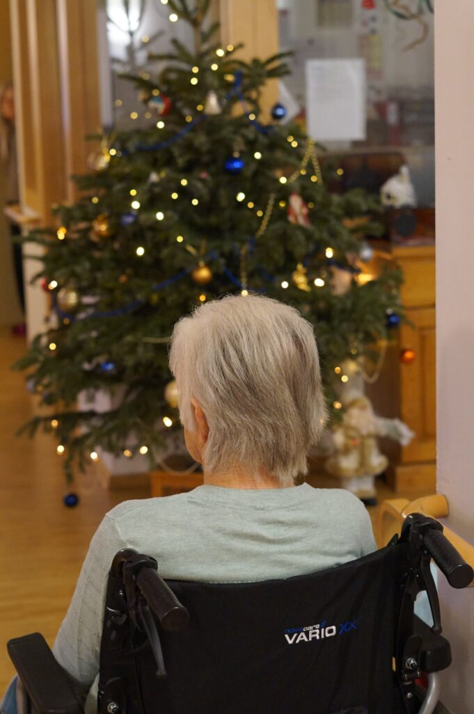 Wie feiert man mit Demenz Weihnachten? Im Pflegeheim oder zuhause. Eine Seniorin vor einem Christbaum.